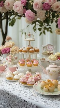 a table topped with lots of cupcakes and pastries next to pink flowers