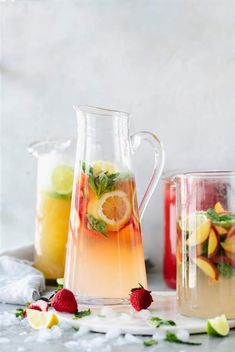 pitchers filled with fruit and lemonade on a white tablecloth next to pitchers