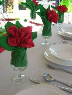 the table is set with white plates, silverware and red flowers in vases