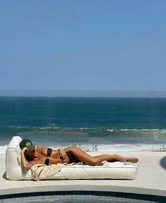 a woman laying on top of a white couch next to a swimming pool near the ocean