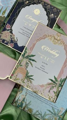 three different colored wedding cards with gold foil and floral designs on them, sitting on green satin