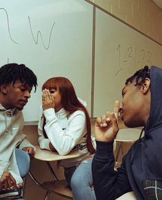 three people sitting at a table in front of a whiteboard with writing on it