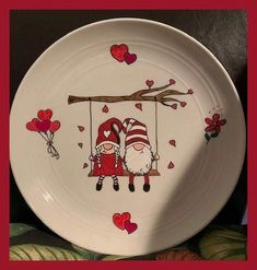 a plate with two gnomes sitting on a swing and hearts flying above them,