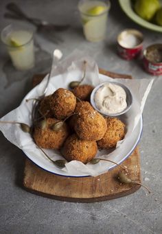 a white plate topped with fried food on top of a wooden cutting board next to cups and sauces