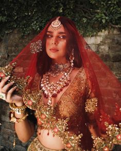 a woman in a red and gold outfit with jewelry on her head, holding a cell phone