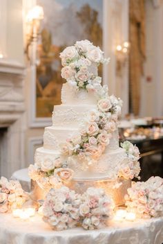 a white wedding cake with flowers on it sitting on a table in front of a fireplace