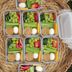 several plastic containers filled with vegetables and dips on top of a grass covered field