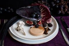 a white plate topped with fruit next to knifes and spoons on top of a purple table cloth