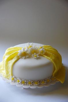 a white cake with yellow icing and daisies on the top is sitting on a plate