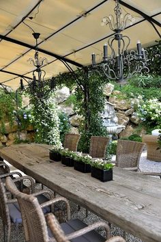 an outdoor dining area with wooden table, chairs and chandelier hanging from the ceiling