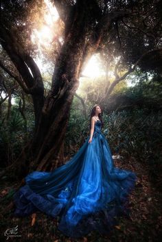 a woman in a blue dress standing under a tree