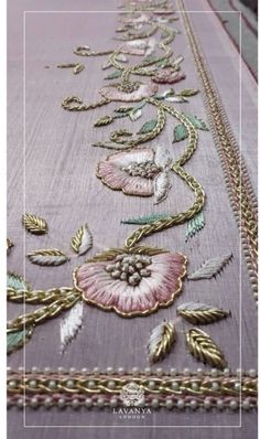 an embroidered table runner with flowers and leaves on the border, along with gold chains