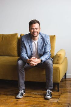 a man sitting on top of a couch in front of a yellow chair with his feet crossed