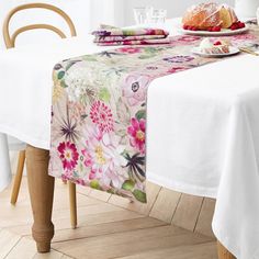 a table topped with a white table cloth covered in pink and green floral designs next to a plate of food