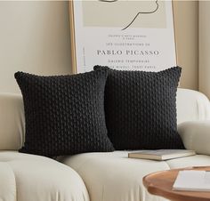 two black pillows sitting on top of a white couch next to a table with a book