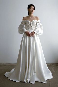 a woman in a white wedding dress standing next to a window with her hands on her hips