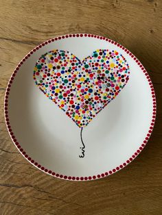 a plate with a heart shaped balloon painted on the front and bottom, sitting on a wooden table