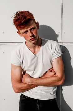 a man with his arms crossed standing in front of a white wall and looking at the camera