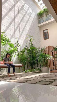 a person sitting on a bench in a room with lots of plants and hanging lights