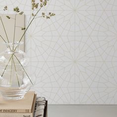 a clear vase filled with flowers sitting on top of a stack of books next to a wallpaper