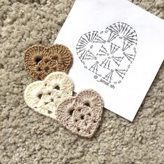 three crocheted hearts sitting on top of a piece of paper next to an envelope