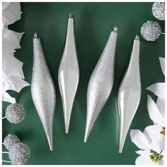 three shiny silver christmas ornaments on a green background with white flowers and poinsettis