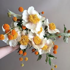 a hand holding a bouquet of flowers with orange and white blooms on it's stems