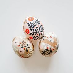 three painted eggs sitting next to each other on top of a white surface with leaves and flowers