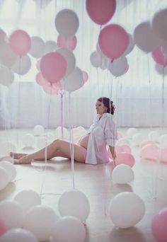 a woman is sitting on the floor surrounded by balloons and streamers in pink and white colors