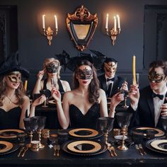 a group of people in masquerades sitting at a table with plates and glasses