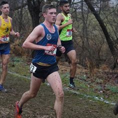 three men running in a cross country race on a muddy trail with trees and bushes behind them