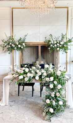 a table with white flowers and greenery on it in front of a chandelier