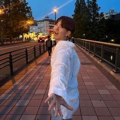 a woman standing on a sidewalk with her hands out to the side and buildings in the background