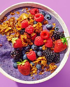 a bowl filled with fruit and granola on top of a purple table next to a pink wall