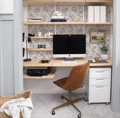 a desk with a computer on top of it in front of a wallpapered wall