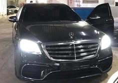 the front end of a black mercedes benz s - class parked in a garage with its lights on