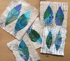 four pieces of paper with blue and green feathers on them sitting on top of a wooden table