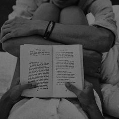 black and white photograph of two hands holding an open book while sitting on a bed