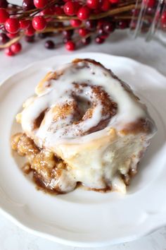 a cinnamon roll on a plate with icing and cranberries in the background