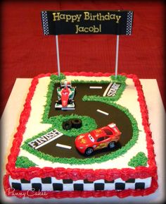 a birthday cake that is shaped like a race track with cars on it and a happy birthday sign