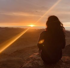 a woman sitting on top of a mountain watching the sun go down in the distance