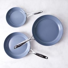 three blue pots and pans with tongs on a white counter top, one is empty