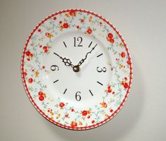 a white clock with red and yellow flowers on it's face hanging from the wall