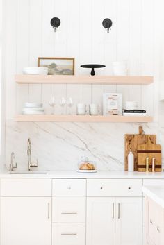 a kitchen with white cabinets and marble counter tops, open shelving above the sink