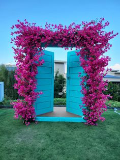 an open blue door with pink flowers on the side and grass in front of it