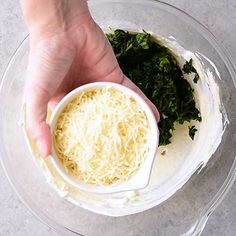 someone is adding cheese and greens to their food in a bowl on top of the counter