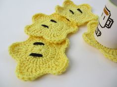 three yellow crocheted coasters sitting next to a coffee cup on a table