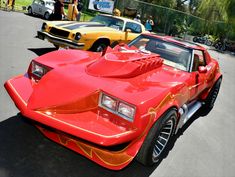 a red car with flames painted on it's hood parked next to other cars