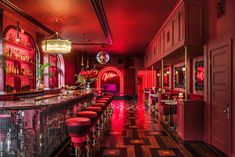 a long bar with red lights and stools at the end is lit up by chandeliers that are hanging from the ceiling