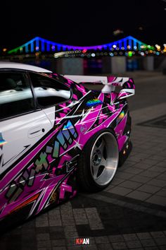 a white car with pink and purple paint on it's side parked in front of a bridge